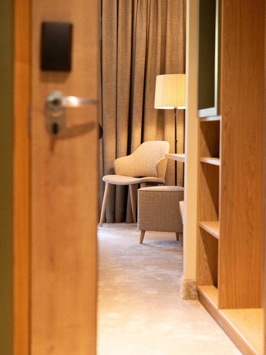 Chambre de l’Hôtel Terra Vinum rénové par l’agence, vue à travers la porte : fauteuil, pouf et dressing en chêne (photo : VieW architecture & décoration)